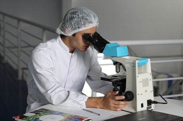 Лаборант в шапочке, смотрит в микроскоп